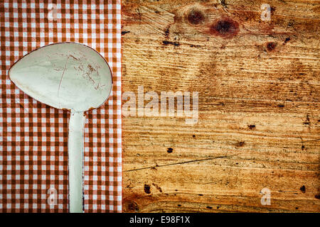 Vieux métal sur une louche de cuisine rouge et blanc rustique formant un tissu vérifié pour une frontière de fond de bois avec copyspace Banque D'Images