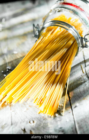 Pot en verre de spaghetti italien couché sur le côté au soleil sur une vieille table de cuisine rustique en bois Banque D'Images