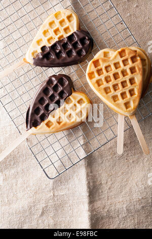 En forme de coeur d'or fraîchement cuits waffle lollipops, certaines avec un enrobage de chocolat sur un rack de grillage métallique dans la cuisine prête pour un parti ou pour une occasion spéciale ou d'un être cher amour Banque D'Images