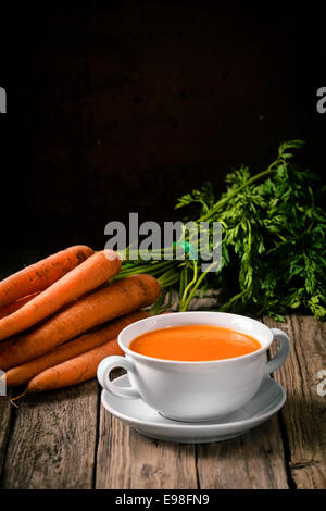 Bol de soupe de carottes chaud maison délicieux avec des ingrédients frais sur un comptoir de cuisine en bois rustique avec copyspace Banque D'Images