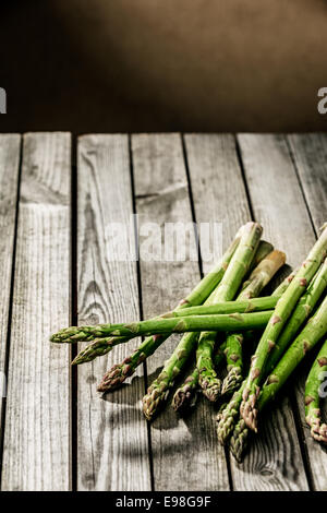 Frais de la ferme fraîchement récolté asperges vertes allongé sur une table en bois rustique dans une cuisine de campagne, avec copyspace Banque D'Images