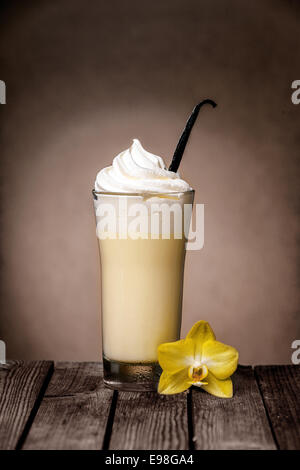 De délicieux milk-shake vanille Glacé recouvert de crème glacée ou crème avec une gousse de vanille pour aromatiser et fleur sur une table en bois rustique Banque D'Images