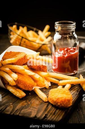 Fried golden crumbed les filets de poisson et frites servi dans un cône de papier avec une sauce à base de tomate ou dip sur une vieille table en bois grunge dans un magasin de poissons Banque D'Images