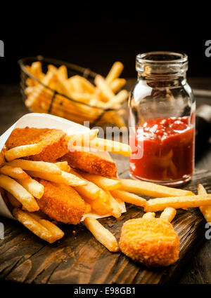 Or croustillant de poisson frit battues portions servi avec des chips de pomme de terre dans une membrane en papier avec une bouteille de ketchup dans une cuisine rustique sur un vieux comptoir en bois Banque D'Images