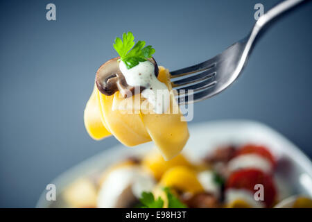 Forkful de Pappardelle aux champignons Nouilles et sauce crème surmonté d'une feuille de basilic frais suspendue au-dessus du reste de la plaque avec l'accent à la fourchette Banque D'Images