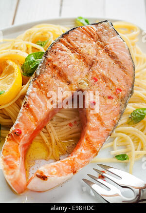 Dîner de fruits de mer d'une table gastronomique escalope de saumon grillé Steak sur pâtes linguine italienne assaisonnée de basilic frais et garnie avec du citron Banque D'Images