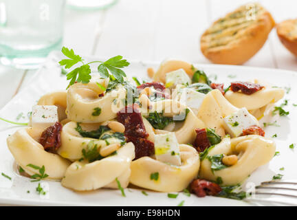 Les pâtes italiennes Tortellini garnies de fromage feta, basilic, noix de pin et les tomates piquantes garni de persil et servi avec des Banque D'Images