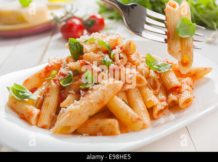 Délicieux salé pâtes penne rigate italien avec le basilic et parmesan râpé servi avec une salade avec une fourche avec deux tubes de pâtes suspendu au-dessus de la plaque Banque D'Images