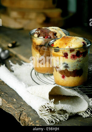 Desserts gâteaux individuels dans des verres avec une variété de fruits avec des baies et un gâteau marbré chocolat et vanille sur une grille de refroidissement sur une toile de jute dans une cuisine rustique de pays Banque D'Images