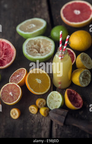 La préparation de pamplemousses frais et jus de citron dans une cuisine de campagne avec une bouteille de jus de fruits fraîchement pressés, entouré de moitié le pamplemousse, citrons, oranges et citrons verts Banque D'Images