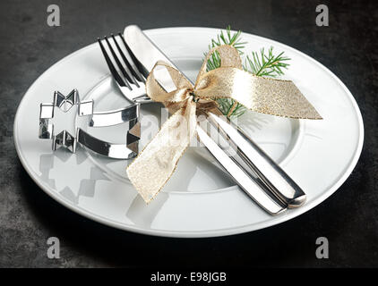 Christmas place setting avec un argent brillant étoile filante emporte-pièce avec un couteau et fourchette attachées avec un ruban d'or de décoration avec un brin de feuillage de pin sur une plaque blanche Banque D'Images