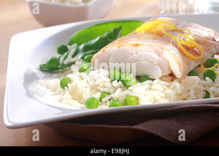 Bon repas de filet de poisson au four garnie de zeste de citron frais, le riz et les pois servi sur une plaque blanche Banque D'Images