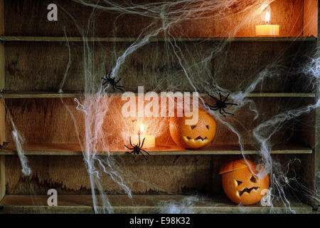 Deux Halloween Jack o lanterne sculptée à partir d'Oranges et d'araignées avec des araignées et allumé des bougies sur des étagères Banque D'Images