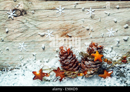 Noel Noël arrière-plan avec des cônes de pin séché drapés dans une guirlande d'étoiles niché sur froid hiver neige avec un fond en bois avec décorations flocon et copyspace Banque D'Images