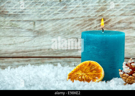 Blue Christmas candle burning colorés en hiver neige avec un cône de pin et de tranche d'orange séchée contre les planches de bois texturés avec copyspace pour votre message d'accueil Banque D'Images