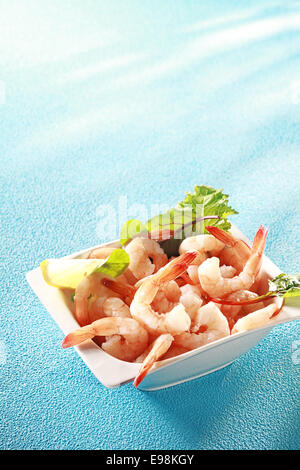 Crevettes crevettes roses fraîches ou apéritif servi avec des tranches de citron et les légumes verts pour une étape gourmande à un repas de début de coquillages, sur bleu Banque D'Images