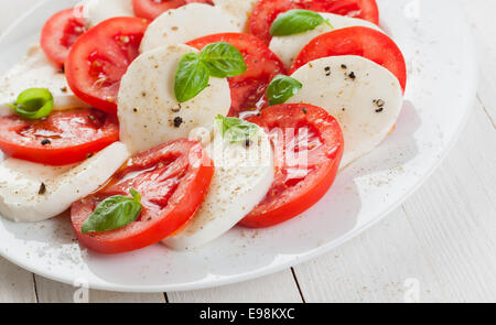 L'Italien tomate et mozzarella salade caprese assaisonné de sel et poivre et garnir de feuilles de basilic frais sur une plaque blanche Banque D'Images