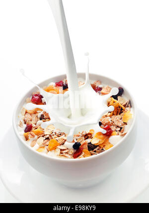 Les projections dans un bol de lait frais de muesli avec un mélange de blé, d'avoine et du son avec des fruits secs et des noix sur fond blanc avec copyspace Banque D'Images