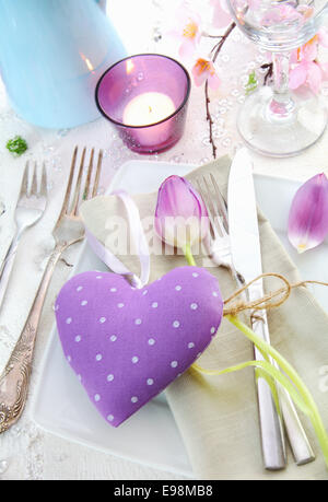 Endroit romantique élégant avec un coeur lilas pour un cœur entouré d'argenterie, d'une bougie et délicates fleurs de printemps Banque D'Images