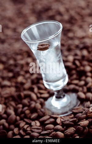 Verre clair dans un grand verre avec grain de café dans le mix, entouré de haricots en grain Banque D'Images