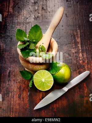 Mortier, limes et de menthe poivrée sur un fond de bois. Ingrédients pour Caipirinha et Mojito Cocktails et autres boissons Banque D'Images