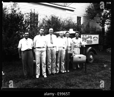 Une photographie montrant six hommes rassemblés autour d'une machine à laver, peut-être entre le début et le milieu du XXe siècle. L'image capture un moment de travail domestique ou industriel. Banque D'Images