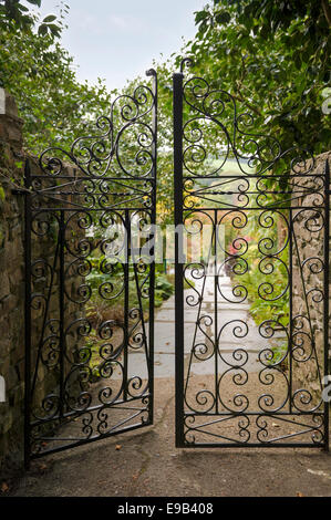 Une paire de portes en fer forgé, conduisant dans un anglais typique, jardin paysager. Banque D'Images