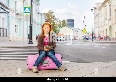 Smiling girl s'asseoir sur le plan de la ville rose avec bagages Banque D'Images