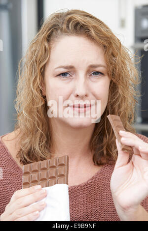 Femme coupable sur le régime alimentaire de manger une barre de chocolat à la maison Banque D'Images