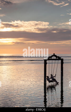 Les touristes sur swing de la mer au coucher du soleil, 'Gili Trawangan, Indonésie, des îles Gili Banque D'Images