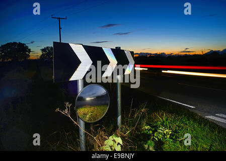 Au crépuscule du trafic passant panneau d'avertissement de virage et de sécurité circulaire miroir pour donner aux conducteurs de voir road uk Banque D'Images