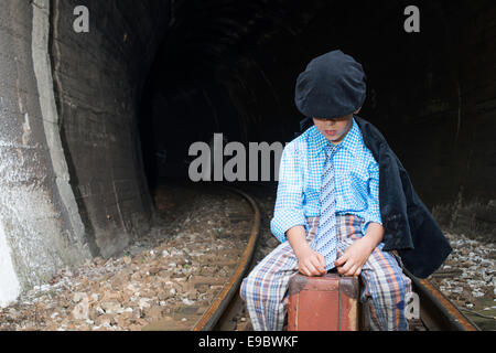 Vêtements vintage dans l'enfant est assis sur la route en face d'un tunnel. Banque D'Images