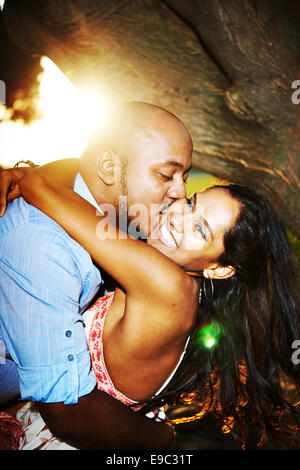 Couple pendant le coucher du soleil par arbre et souriant et serrant Banque D'Images