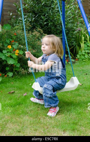 Deux ans, fille, jouant sur une balançoire dans un jardin. UK. Banque D'Images