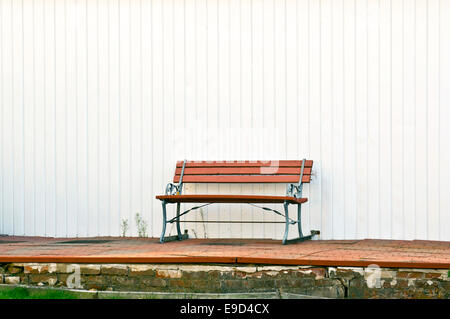 Un seul banc de parc en bois rouge sur un patio extérieur en face d'un mur blanc c'est éclaboussé de peinture rouge derrière le banc Banque D'Images