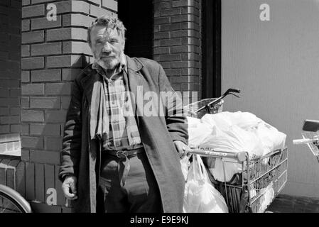 Un sans-abri avec toutes ses affaires dans des sacs en plastique dans un chariot de supermarché Tesco 90 Angleterre southsea Banque D'Images