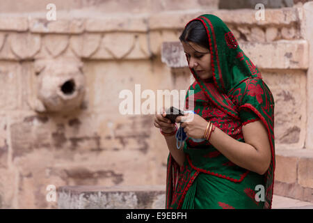 Femme portant un sari rouge vert avec des décorations à la recherche à son téléphone mobile. Mehrangarh, Jodhpur, Rajasthan, India Banque D'Images