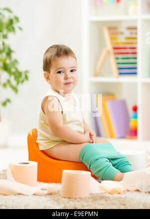 Smiling enfant assis sur le pot de chambre avec du papier toilette Banque D'Images