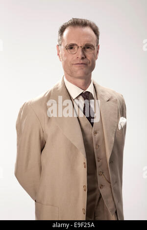 Homme d'âge moyen appris en costume pâle avec des lunettes aux gestes tout en parlant d'une photo d'action prises sur un fond blanc. Banque D'Images