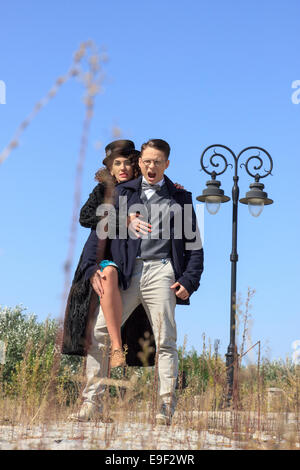 Homme en colère debout à côté de sa femme rétro à la mode sur vintage road par le lampadaire Banque D'Images