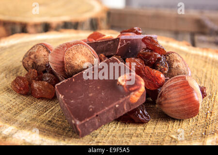 Barres de chocolat aux noix et raisins secs sur souche en bois parfait, pile de pièces en chocolat avec des raisins secs et de noisettes Banque D'Images