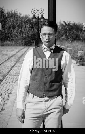 L'homme à veste et bowtie comité permanent par le chemin de fer appuyé contre lampadaire en vieille ville vintage en noir et blanc Banque D'Images