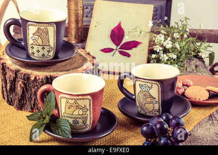 Trois tasses de thé vides on retro table en bois à côté de l'écorce d'un arbre avec les cookies et de raisin à côté de Banque D'Images