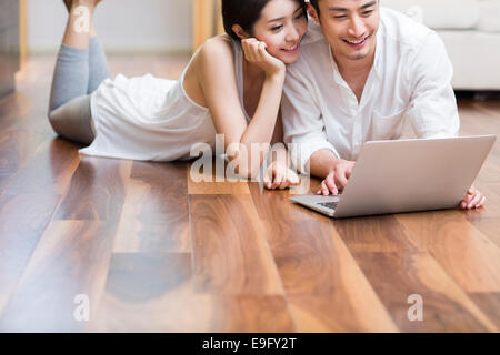 Jeune couple lying on floor using laptop Banque D'Images