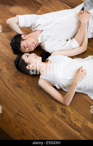 Young couple holding hands lying on wooden floor Banque D'Images