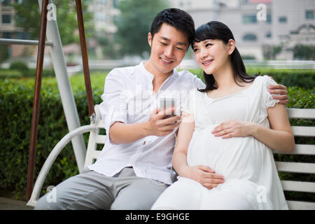 Jeune homme et femme enceinte l'écoute de musique sur balançoire Banque D'Images