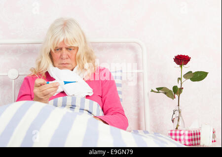 Femme malade en pyjama rose à au thermomètre, avec des tissus, de la rose et une débarbouillette Banque D'Images