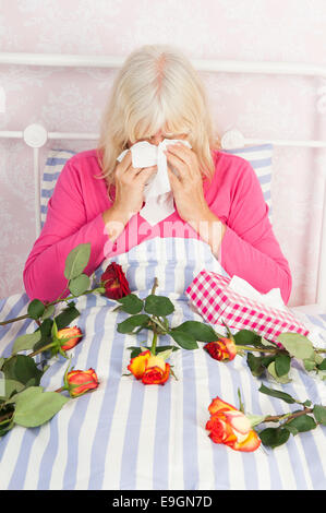 Femme triste en pyjama rose assis au lit avec un bouquet de roses et de tissus Banque D'Images