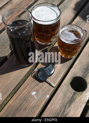 Clés de voiture avec une boisson gazeuse et pintes de bière sur une table de jardin en bois Banque D'Images