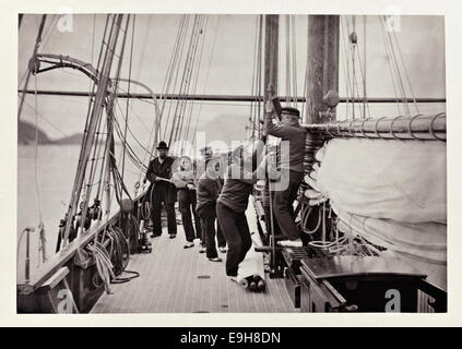 Cette image représente le levage de la voile principale à bord du navire 'Nereid' lors de sa croisière de 1869. La photographie capture un moment historique de l'histoire maritime, en se concentrant sur les techniques de voile de l'époque. Banque D'Images